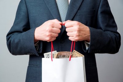 Mężczyzna w garniturze trzyma w rękach torbę wypełnioną banknotami
