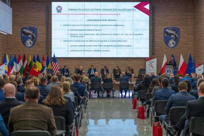 Uczestnicy międzynarodowej konferencji oraz uczestnicy panelu dyskusyjnego. W tle duży ekran z informacją o tematyce konferencji.