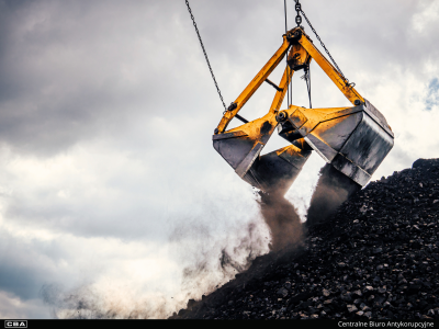 Składowisko węgla kamiennego, zbliżenie na chwytak dźwigu, w tle pochmurne niebo.
