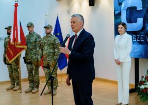 Mr Tomasz Siemoniak, Minister of the Interior and Administration, Coordinator of Special Services speaks to the microphone. The Head of the CBA and three CBA officers stand in the background. One of the officers holds a Polish emblem.