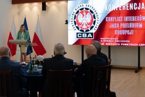 The Head of the CBA, Ms Agnieszka Kwiatkowska-Gurdak speaks in front of the attendees. In the background, a screen with the caption Conference ‘Conflict of interest as a prelude to corruption’ and the CBA logo.