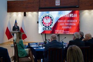 The speaker speaks in front of the audience. In the background, a screen with the words Conference ‘Conflict of interest as a prelude to corruption’ and the CBA logo.