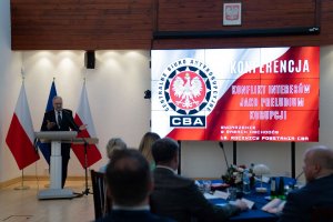 The speaker speaks in front of the audience. In the background, a screen with the words Conference ‘Conflict of interest as a prelude to corruption’ and the CBA logo.