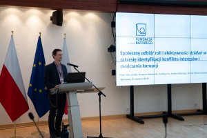 A speaker from the Stefan Batory Foundation speaks to the audience. In the background a presentation screen with the caption: ‘Public perception of the role and effectiveness of efforts to identify conflicts of interest and combat corruption’.