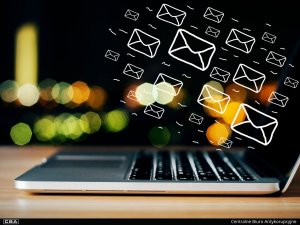 Photo of a laptop on a desk. The iconography of envelopes above it.