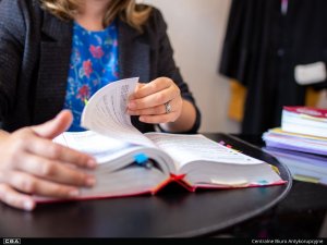 A woman sits at a table and browses through a Code. A lawyer’s robe hangs in the background.