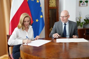 Deputy Head of the CBA Dariusz Drozdowski and Secretary of State of the Ministry of Education Joanna Mucha sit at the table and sign an agreement.