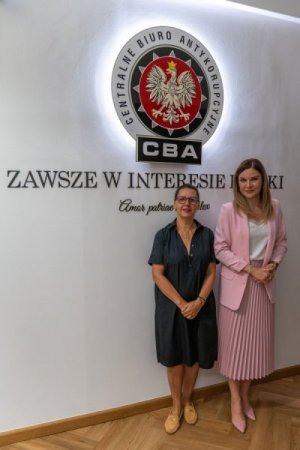 Agnieszka Kwiatkowska-Gurdak and Magdalena Pawlak pose for a photo. CBA’s emblem and inscription „Always in the interest of Poland” on the wall.