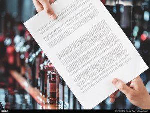 two hands holding one document, in the background a cabinet with bottles of alcohol