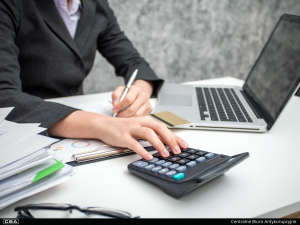 A person in a suit using a calculator at a desk with a laptop