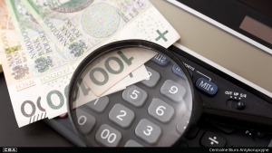 a calculator and polish banknotes on the table, with a magnifying glass on them