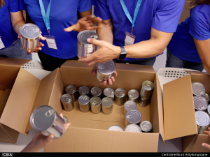 People in blue shirts packing canned food into cardboard boxes, preparing aid supplies.