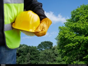 Worker in a high-visibility vest holding a yellow hard hat outdoors.