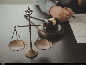 Scales of justice and a judge’s gavel on a table in the background, along with documents