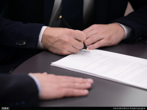Men sitting at a table signing a document.